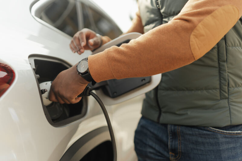 Young multiracial man charging his electric car, close-up.