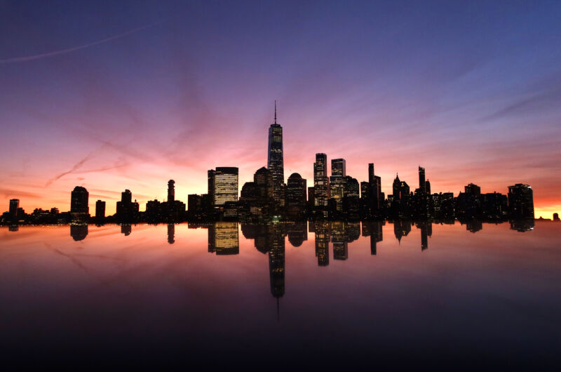 Lower Manhattan and One World Trade Center in New York City are reflected on a monument as the sun rises on December 22, 2023, as seen from Jersey City, New Jersey.