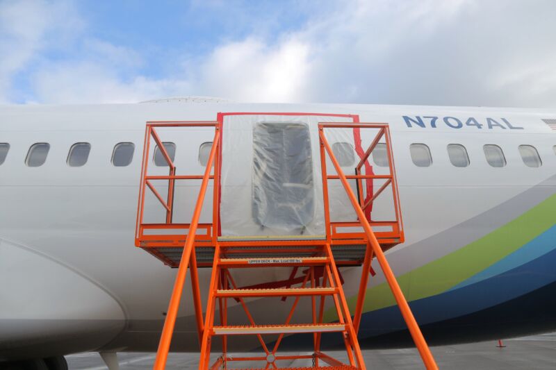 Tarp-like material covers a large opening in the side of a Boeing airplane.