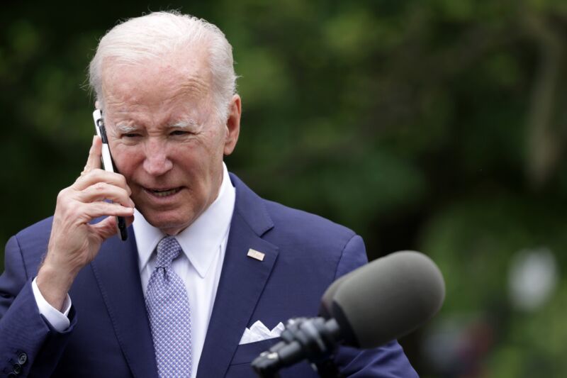 Joe Biden holds a cell phone to his ear while having a conversation.