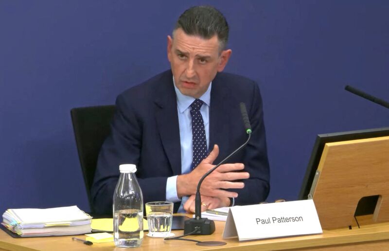 Paul Patterson, co-CEO of Fujitsu's European division, sits at a table in front of a microphone while testifying for a public inquiry.