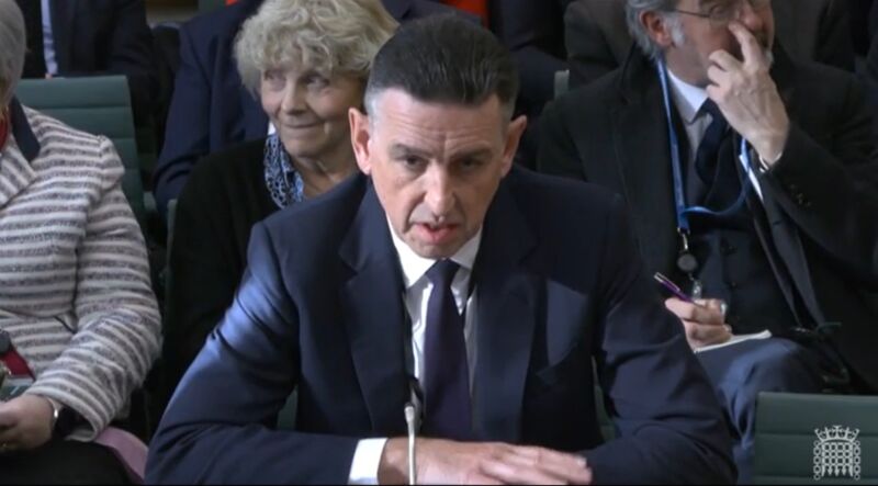 Fujitsu executive Paul Patterson sits at a table and speaks into a microphone while testifying at a Parliament hearing.