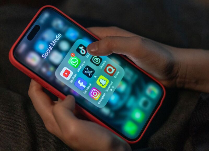 Las manos de un niño sosteniendo un iPhone que muestra los íconos de varias aplicaciones de redes sociales, incluidas YouTube, Facebook, X, TikTok e Instagram.