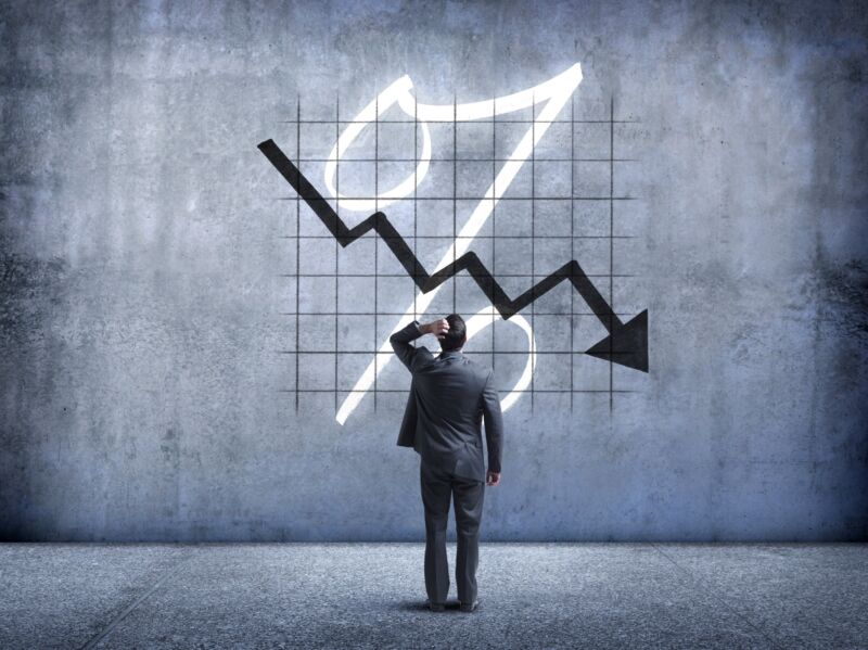 Un hombre de negocios se pone la mano en la cabeza mientras mira hacia arriba y queda perplejo ante un gráfico que indica una caída en el valor.