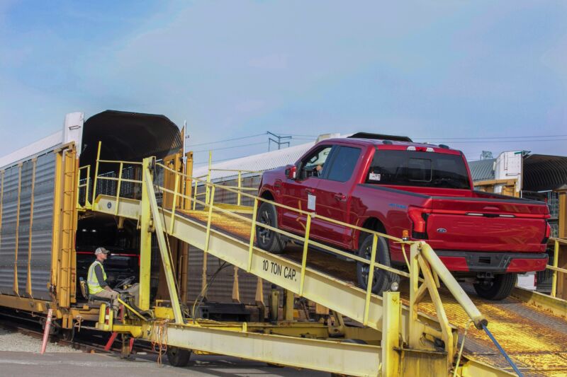 A red F-150 Lightning being loaded onto a train car for transport.