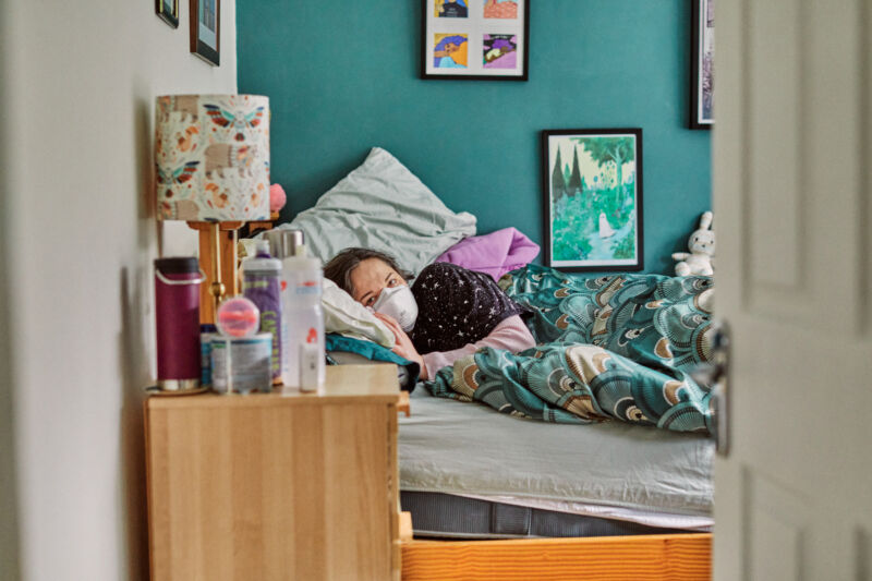Una mujer con COVID prolongado que se encuentra completamente postrada en cama, requiriendo el uso de silla de ruedas para desplazarse entre las habitaciones de su casa. 