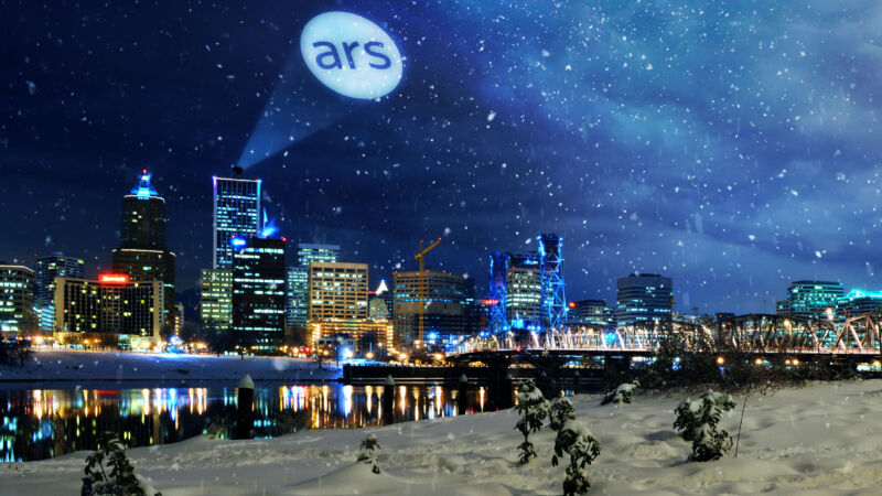A spotlight shines the Ars signal in the sky over snowy Portland