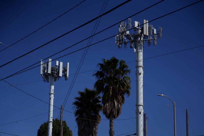 A picture of two cellular towers. Trees and aerial power lines are also in the photo.