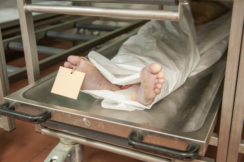 image of a covered corpse with feet exposed on a metal table in a morgue