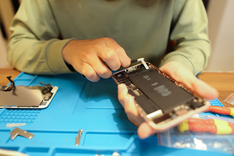 Se retira la batería del iPhone de un iPhone sobre una alfombra de reparación azul
