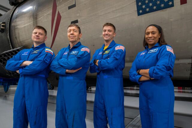 El cosmonauta ruso Alexander Grebenkin, el piloto Michael Barratt, el comandante Matthew Dominick y la astronauta Jeanette Epps posan con un cohete Falcon 9 dentro del hangar de SpaceX en Florida.