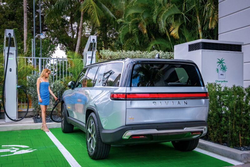 A woman plugs a Rivian SUV into a fast charger.