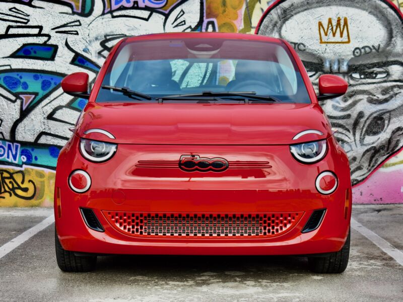 Una foto frontal de un Fiat 500e rojo frente a un mural.