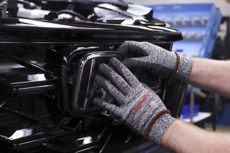 A worker applies a Honda badge to the front of a Honda vehicle