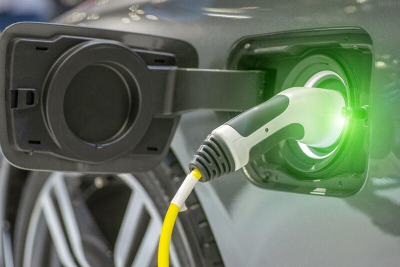 A charging cable plugged in to a port on the side of an electric vehicle. The plug glows green near where it contacts the vehicle.
