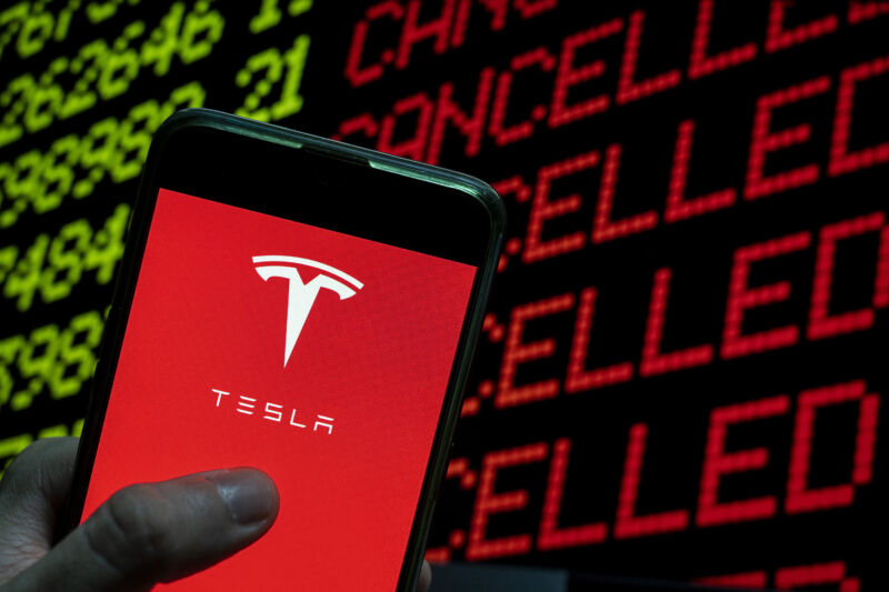 In this photo illustration the American electric car manufacturing company brand Tesla logo is seen on an Android mobile device with a computer key which says cancel and cancelled
