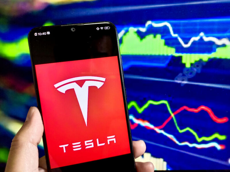 A cellphone showing the Tesla logo with a stock chart in the background