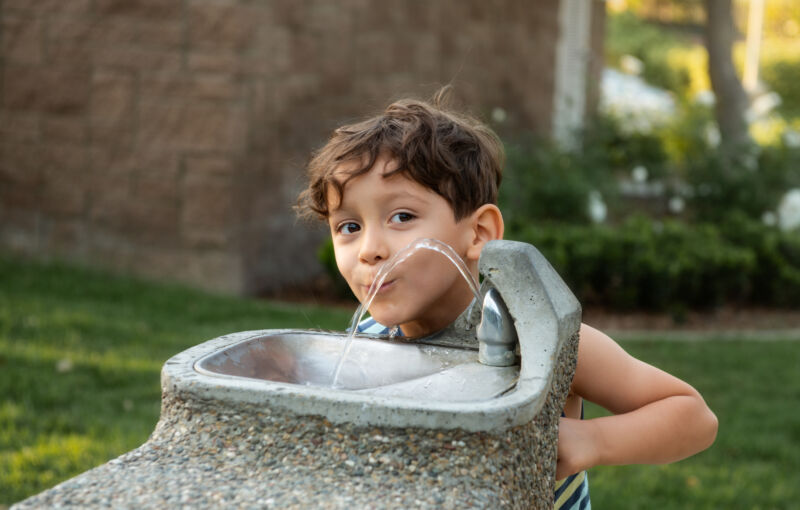 A young person drinks from a public water fountain.