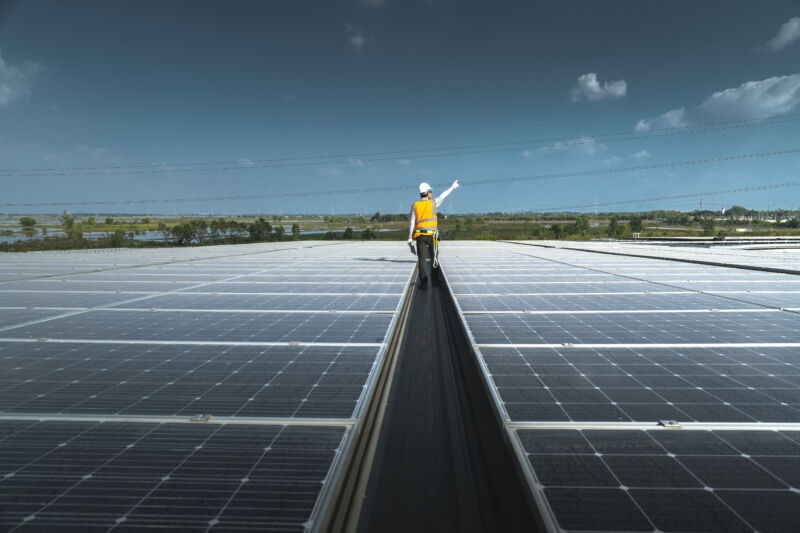 A worker walks between long rows of solar panels.