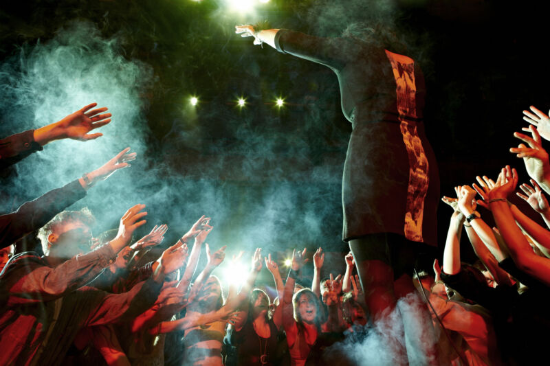 A female singer gestures towards an enthusiastic crowd.