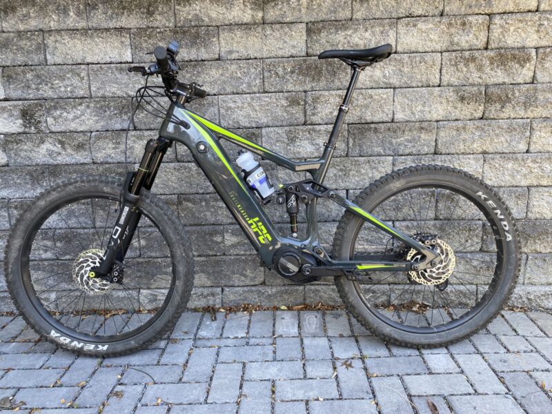 Imagen de una gran bicicleta de montaña de color verde oscuro contra un muro de piedra gris.