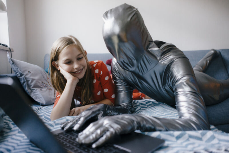 Man in morphsuit and girl lying on couch at home using laptop
