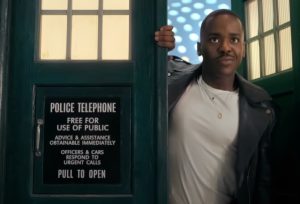 Gatwa in white t shirt jeans and black leather jacket standing in doorway of the TARDIS