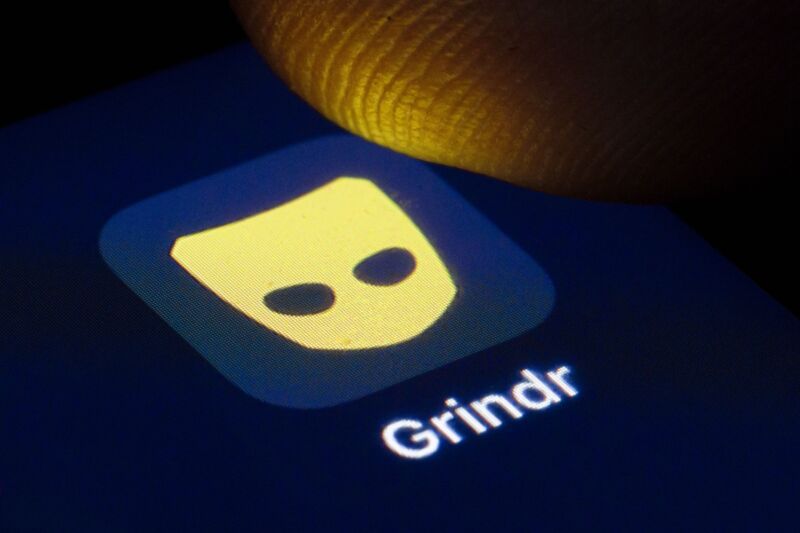 A person's finger hovering over a Grindr app icon on a phone screen