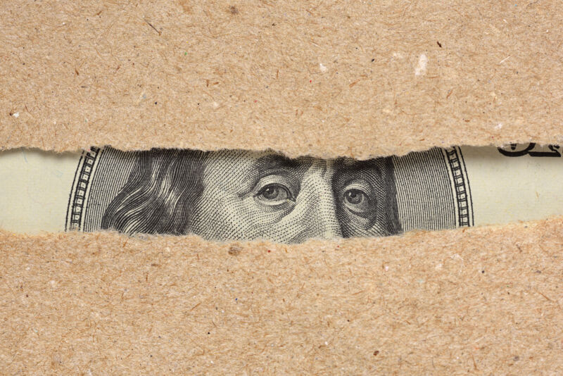 Un Billete de cien dólares Retrato de Benjamin Franklin asomándose detrás de un papel marrón roto