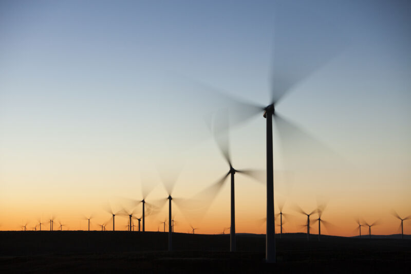 Wind turbines in front of a sunrise, with their blades blurred due to their motion.