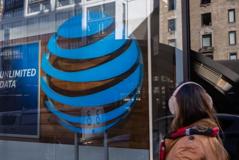 A pedestrian walks past a large AT&T logo on the glass exterior of an AT&T store.