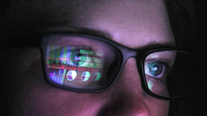 A person using a computer with a computer screen reflected in their glasses.