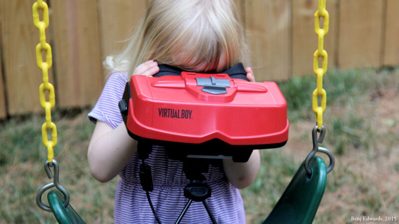 A young kid using a Virtual Boy on a swing.