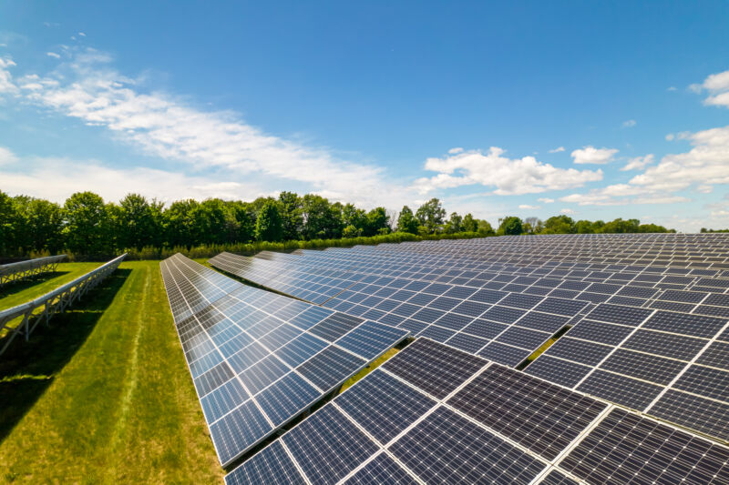 Imagine cu panouri solare pe un câmp verde cu iarbă, cu cerul albastru în fundal.