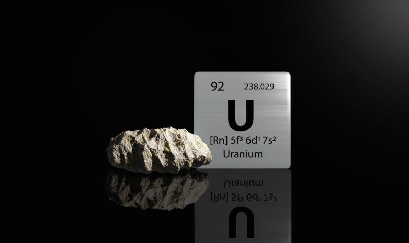 A lump of rock, next to the periodic table entry for uranium, all against a black background.