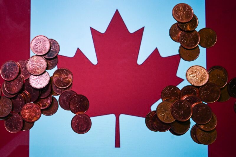 Illustrative photo featuring Canadian 1-cent coins with the Canadian flag displayed on a computer screen in the background,