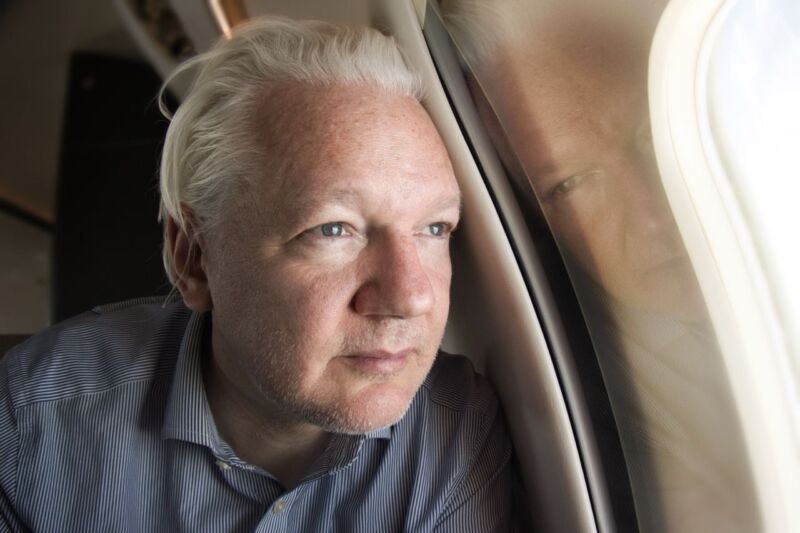Julian Assange in an airplane seat, looking out the window.