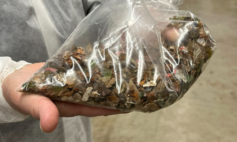 Image of a person holding a bag full of dirty looking material with jagged pieces in it.