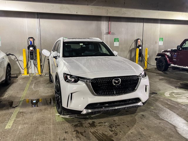 A white Mazda CX-90 charges in a parking lot