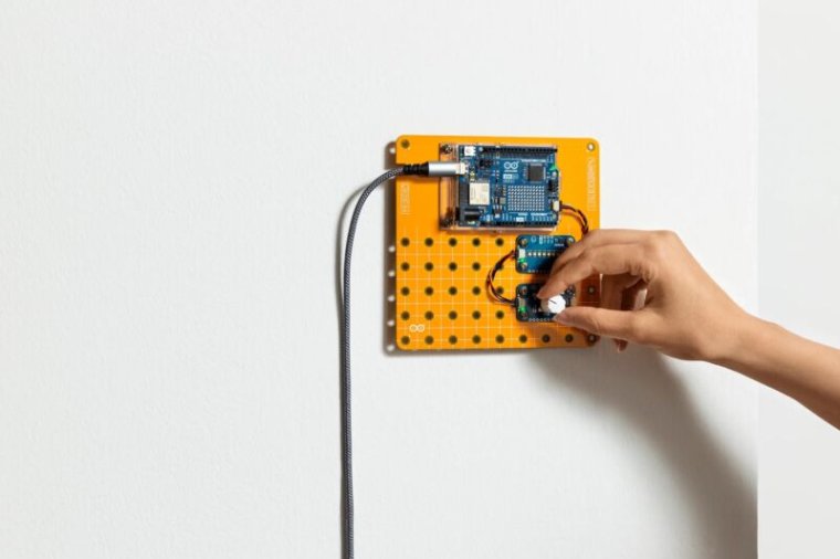 A hand adjusting a button or knob on an Arduino plug and make kit, mounted to a white whall on a yellow bread-board-like backing.