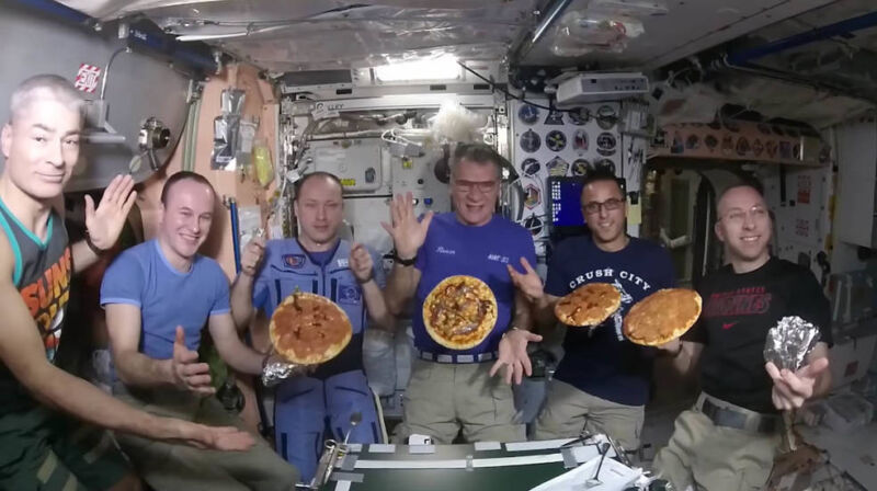 Image of astronauts aboard the ISS showing off pizzas they've made.
