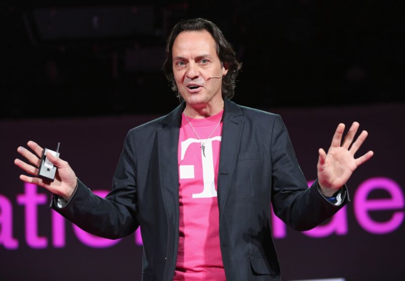 Then-CEO of T-Mobile John Legere speaking at an event, wearing a sports jacket and T-Mobile t-shirt.