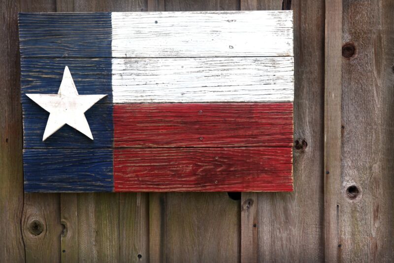 A Texas flag painted on very old boards and hanging on a barn.