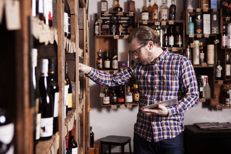 Man looking over the offerings at a wine store with a tablet in hand.