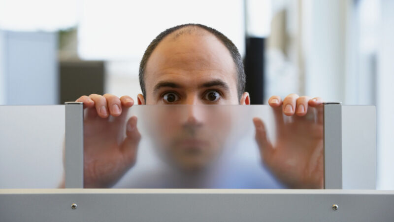 A man looks over a glass partition, searching for transparency.