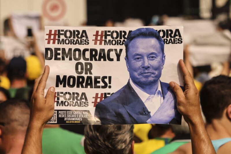 A supporter of former Brazil President Jair Bolsonaro holds a sign that has a picture of Elon Musk and the text, 