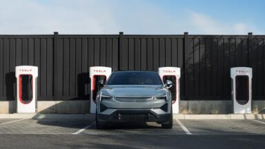 A Polestar 2 EV parked in front of a bank of Tesla Superchargers