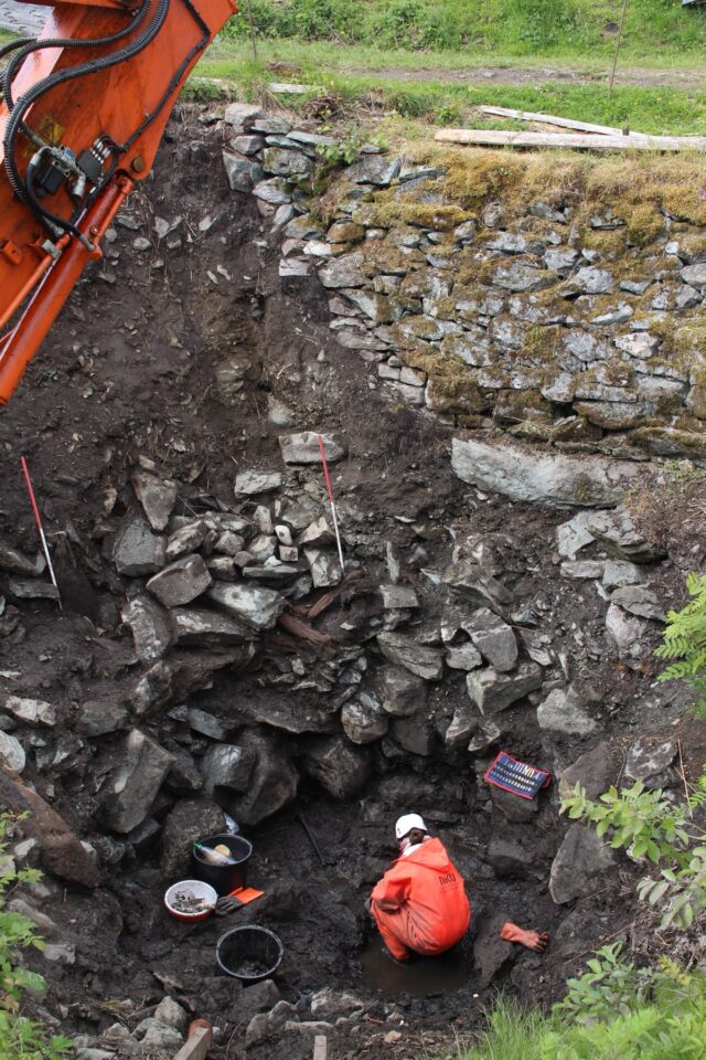 worker in hard hat and orange jacket excavating an archaeological site