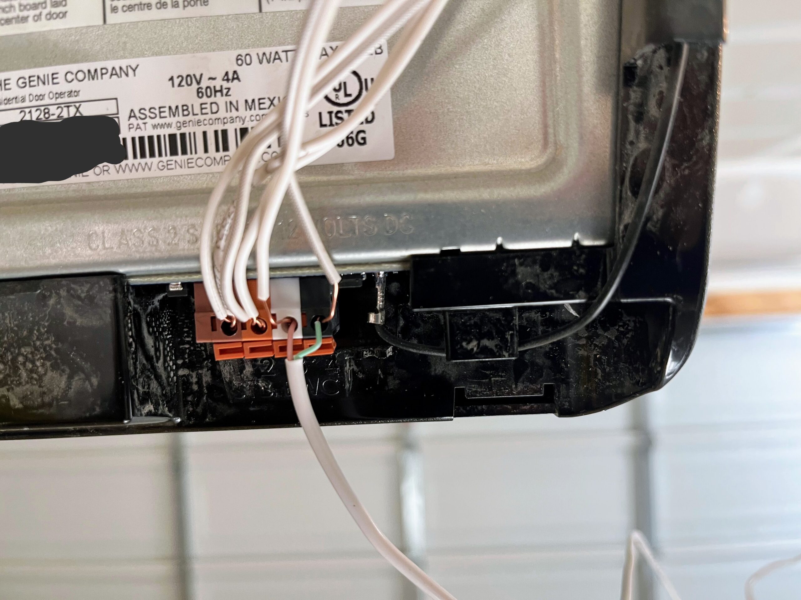 Wires running from terminal points in the back of a garage door opener, with one set of wires coming in from the bottom and pressed into the same press-fit holes.