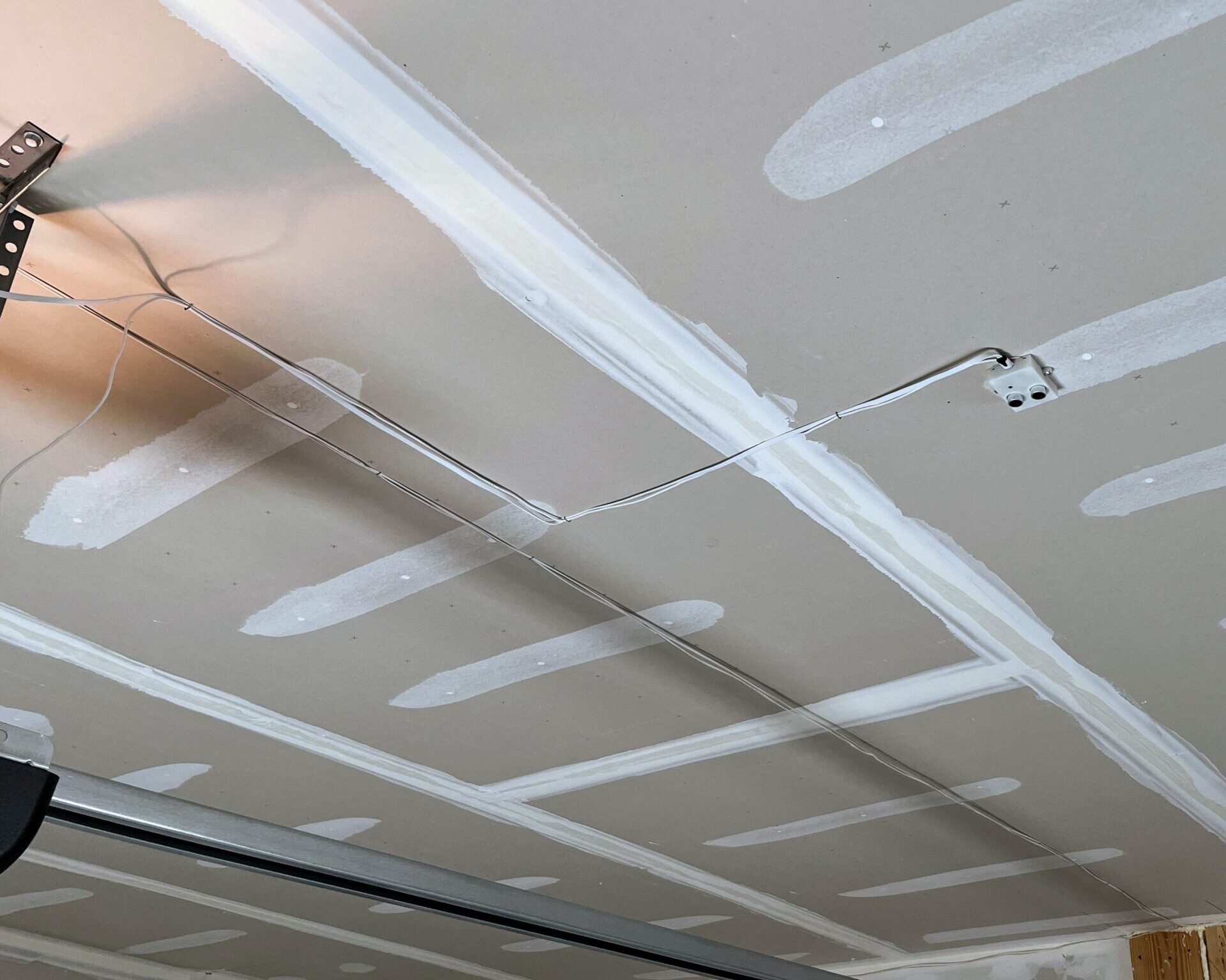 A garage ceiling, with drywall stud paint running across, a small device with wires running at right angles to the opener, and an opener rail beneath.